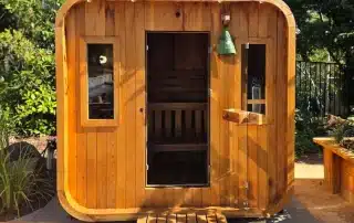 Outdoor wooden sauna cabin with curved edges, front door open showing interior benches and warm wood tones.